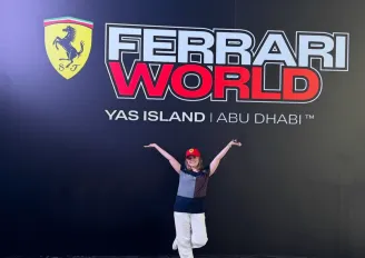 Girl stood in front of Ferrari World sign which has black background, red and white text and the Ferrari logo next to the name.